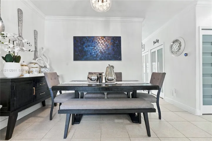 Dining area featuring neutral tile flooring, crown molding, and a spherical glass-shade pendant light