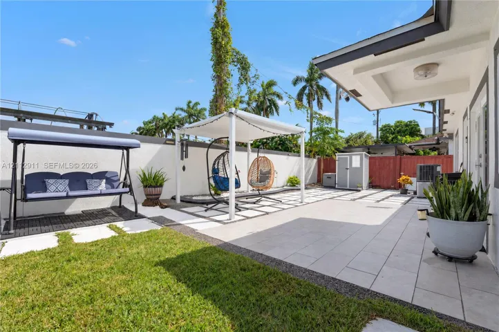 Backyard featuring a paved patio with geometric stone inlay, a covered pergola structure, a solid perimeter wall, and a maintained lawn area