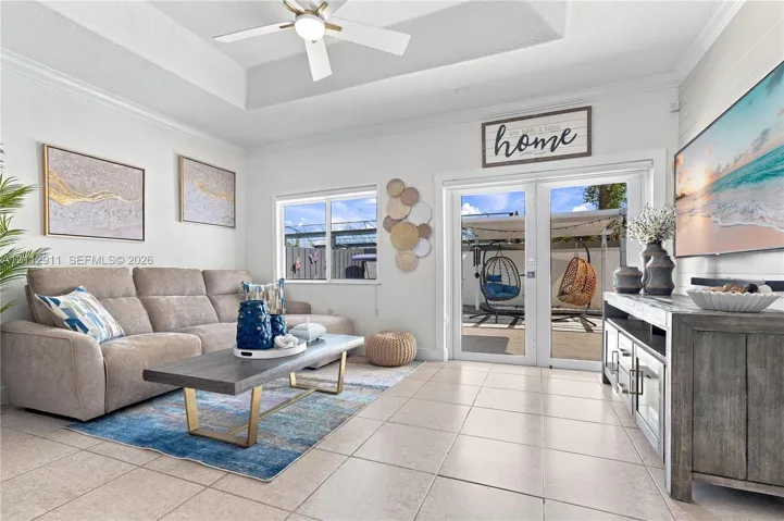 Living area featuring a tray ceiling, ceiling fan, neutral ceramic tile flooring, and glass-paned double doors