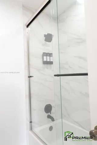 Shower enclosure featuring large-format tile surround, glass sliding door, and matte black shower fixtures