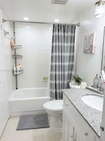 Bathroom featuring a vanity with a light-toned speckled countertop, an integrated sink, white cabinetry, a porcelain tub-and-shower combination with tiled surround, and recessed ceiling lighting