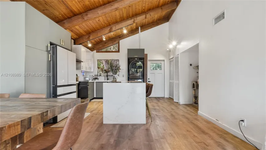Vaulted ceiling with exposed wood beams, wood-finish flooring, central island featuring a quartz countertop, and white cabinetry