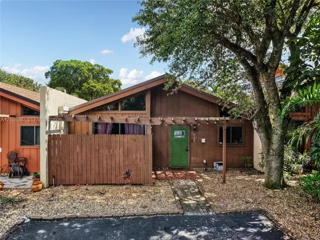 Exterior featuring a gabled roofline, wood-paneled siding, a decorative timber pergola, and a brick-paved entry path