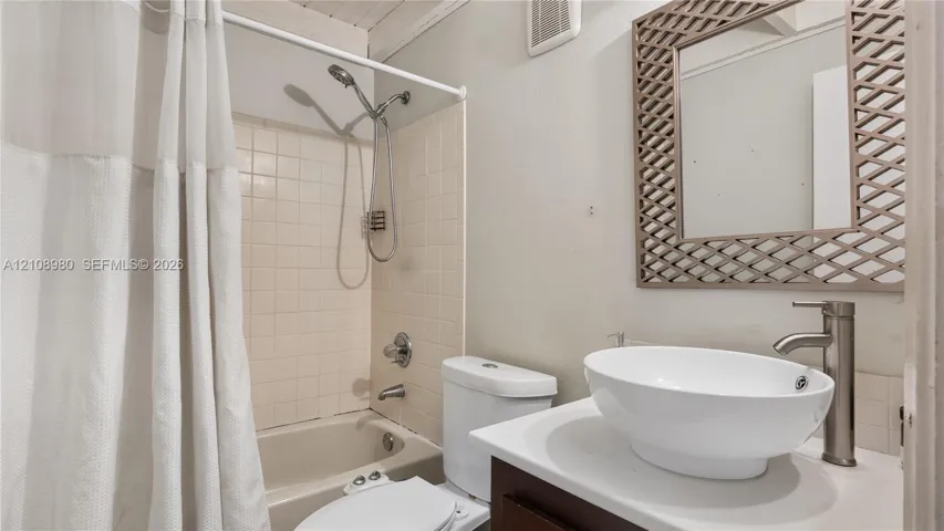 Bathroom featuring a vanity with a white vessel sink, a tall metallic faucet, a tiled shower-tub combination with a handheld showerhead, and a framed mirror