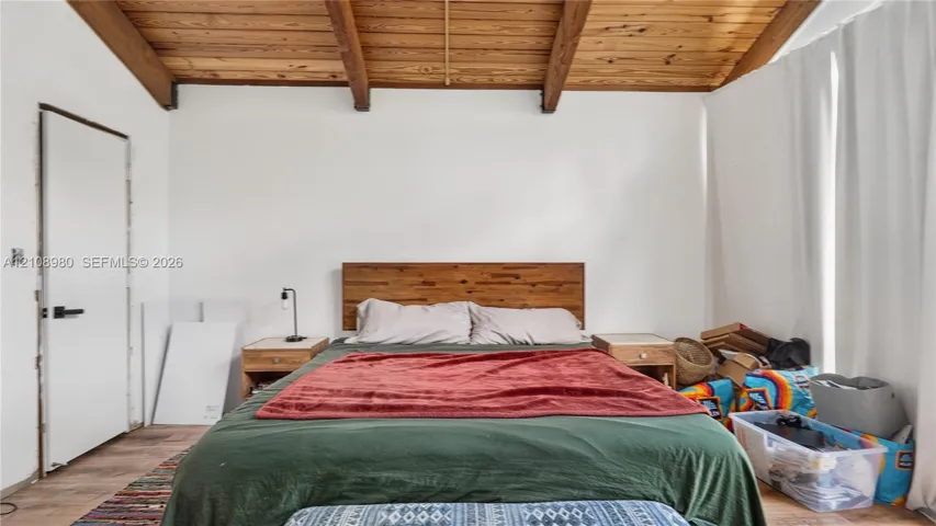 Vaulted ceiling featuring exposed wood beams, wood-finish flooring, and a flat-panel interior door with matte black hardware
