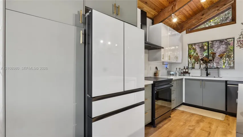 Kitchen featuring two-tone cabinetry with metallic hardware, integrated refrigerator, exposed wood-beam vaulted ceiling, and wood-finish flooring