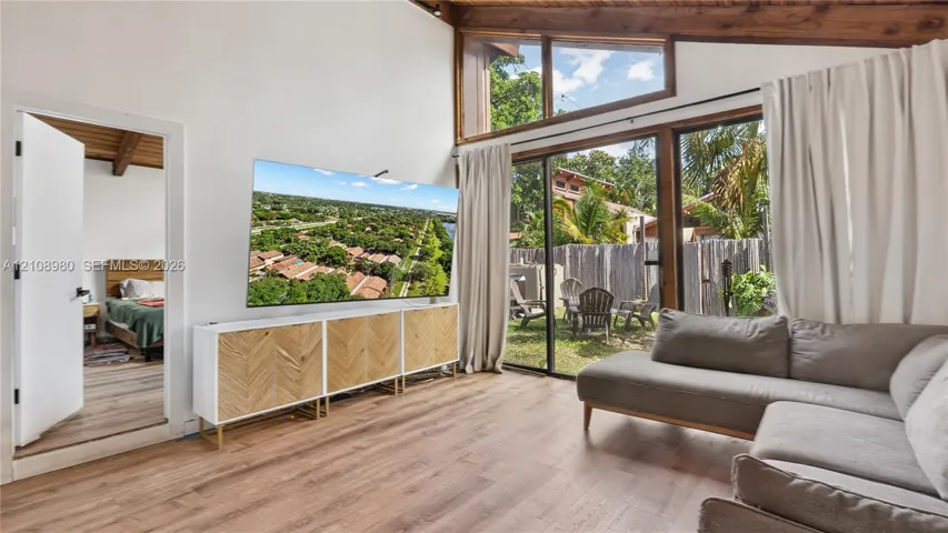 Vaulted ceilings with exposed timber beams, expansive floor-to-ceiling windows, wood-finish flooring, and sliding glass doors