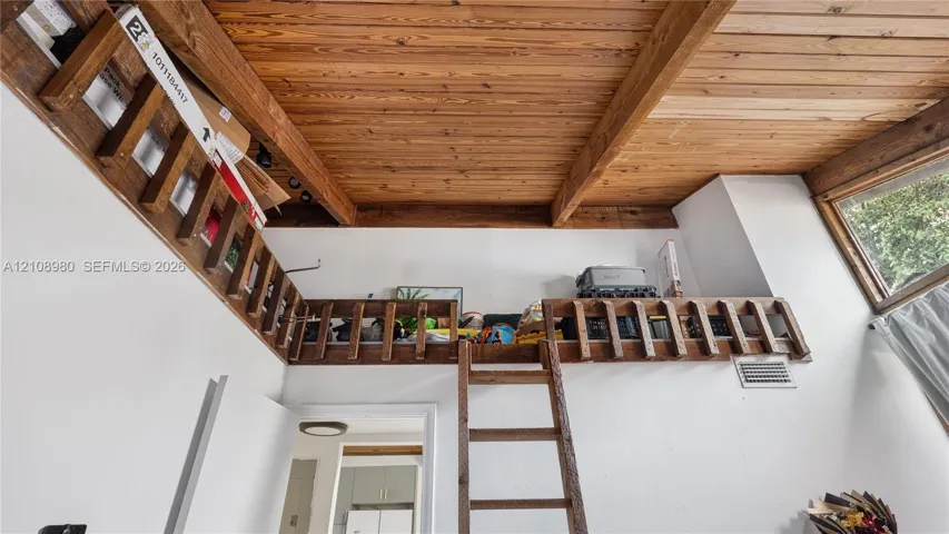 Interior space featuring high ceilings with exposed wood beams and wood-plank ceiling finish, an elevated wooden loft platform with integrated wood railings, and a wooden ladder