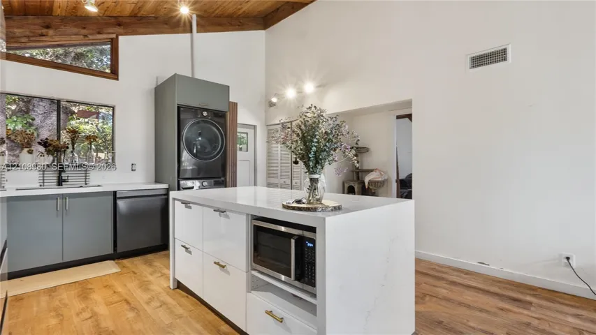 Vaulted ceiling featuring exposed wood beams, center island with stone-surface countertop, wood-finish flooring, matte-finish cabinetry, and stainless steel built-in appliances