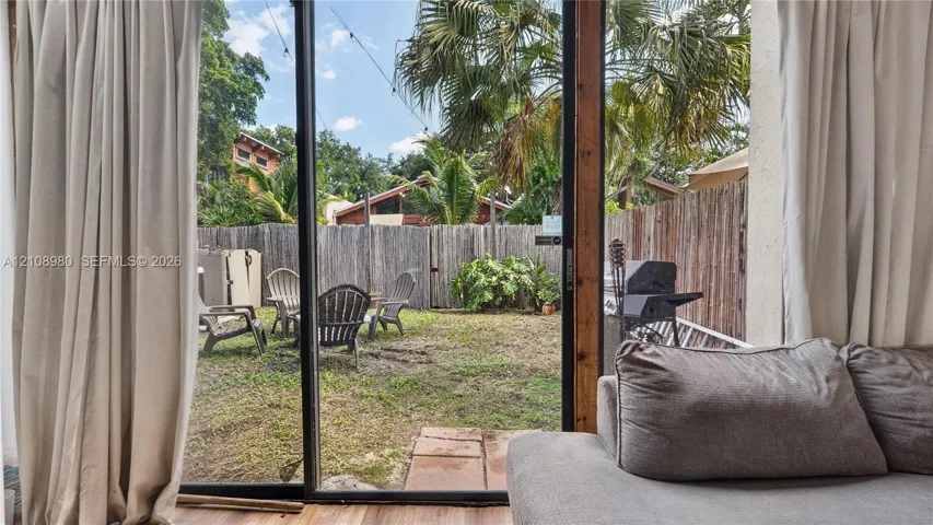 Sliding glass door opening to a private backyard enclosed by wood fencing, featuring stone pavers and mature palm trees