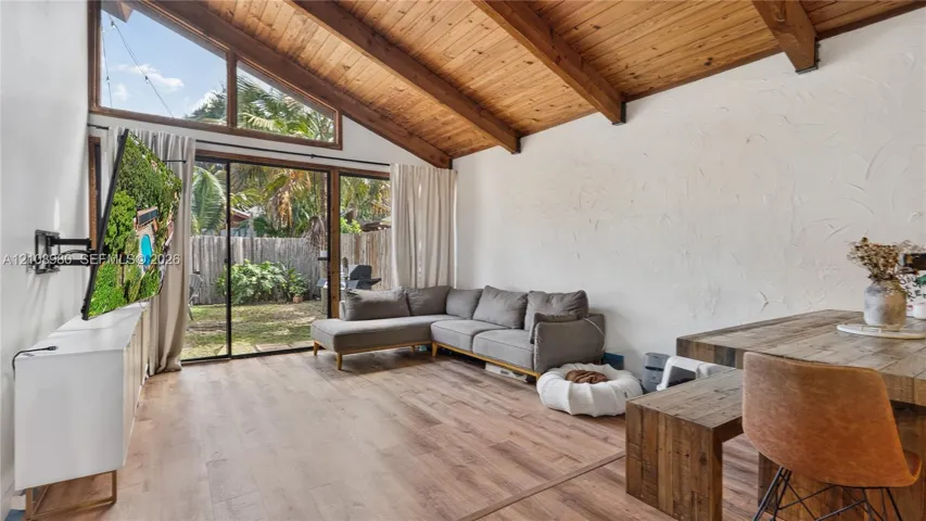 Vaulted ceilings featuring exposed wood beams, wood-finish flooring, and expansive windows with sliding glass doors
