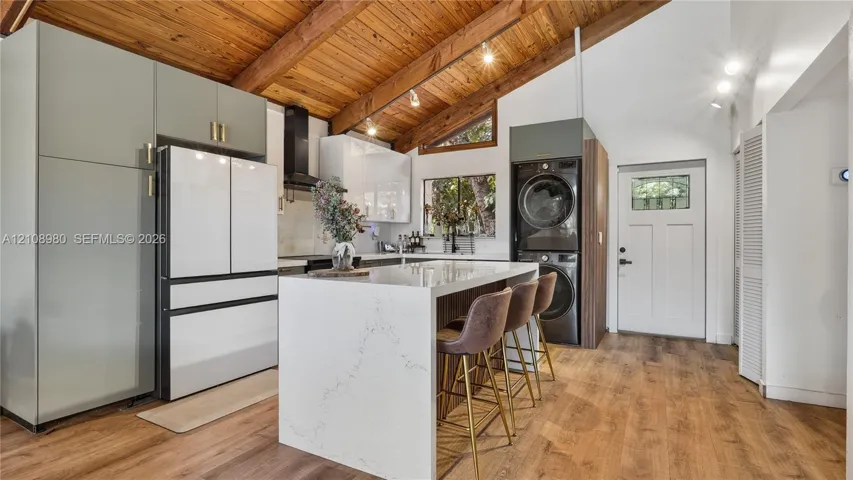 Kitchen featuring a vaulted ceiling with exposed wood beams, center island with stone-finish countertop, flat-panel cabinetry, and integrated laundry appliances