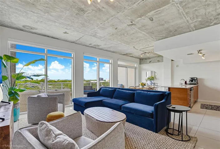 Exposed raw concrete ceiling, floor-to-ceiling windows, large-format tile flooring, and integrated kitchen island