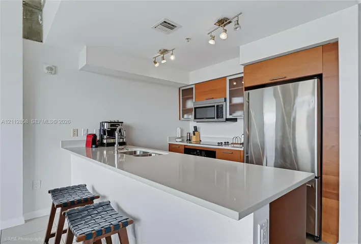 Kitchen featuring a quartz countertop, stainless steel refrigerator, microwave, and range, with wood-finish cabinetry and overhead track lighting