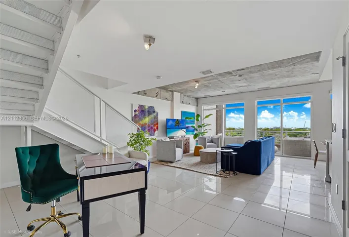 Open-concept interior featuring polished tile flooring, industrial-style exposed concrete ceiling, staircase with metal railing, and floor-to-ceiling glass panel doors