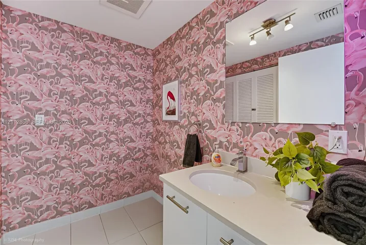 Bathroom featuring patterned wall covering, solid-surface vanity countertop, undermount oval sink, polished metal fixtures, and large-format tile flooring