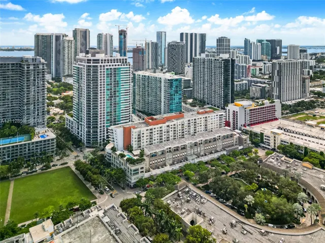 Aerial perspective featuring a mid-rise residential building with an elevated outdoor pool, expansive green space, and urban skyline backdrop