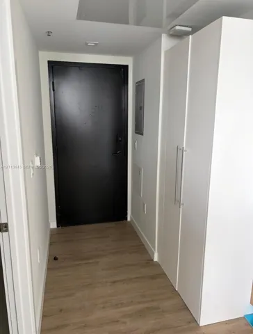 Entryway featuring wood-finish flooring, a matte black door, and built-in floor-to-ceiling cabinetry with stainless steel pulls