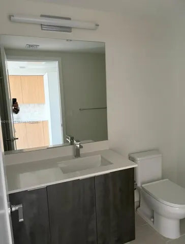 Modern vanity with a rectangular sink, stone-surface countertop, high-contrast cabinetry, large wall-mounted mirror, and linear light fixture