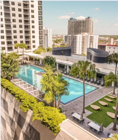 Rooftop swimming pool featuring a lap lane, surrounding wood-finish decking, integrated landscaping, and manicured green space