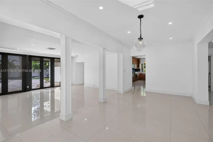 Open-concept interior featuring large-format polished tile flooring, recessed lighting, architectural columns, and dark-framed glass paneled doors