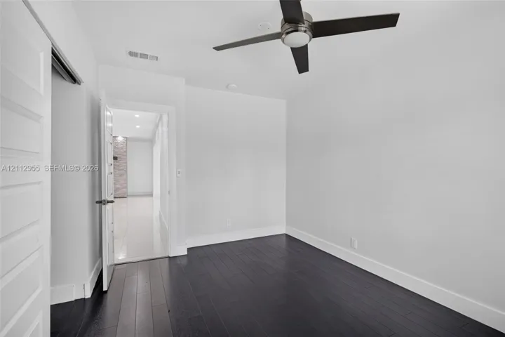 Room featuring dark wood-finish flooring, a multi-blade ceiling fan with integrated lighting, and a solid-core interior door