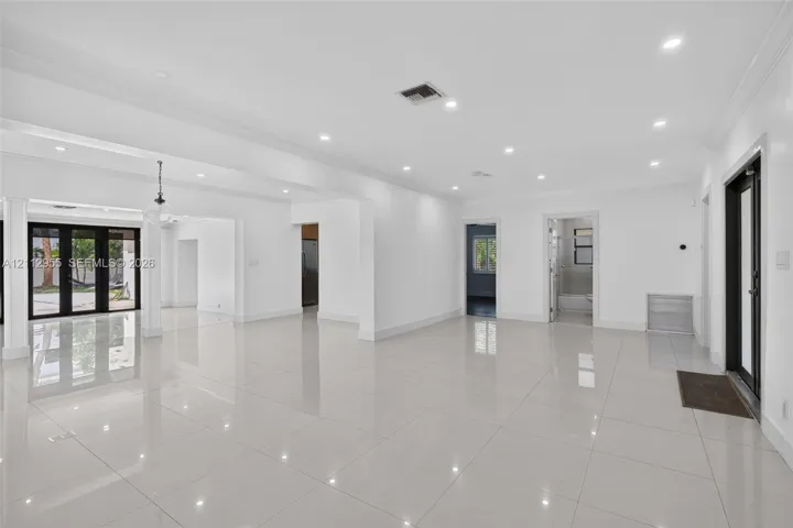 Open-concept interior featuring large-format tile flooring, recessed ceiling lighting, crown molding, and black-framed glass patio doors