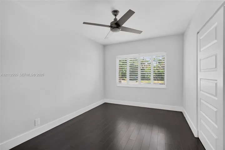 Room featuring wood-finish flooring, plantation shutters, and a four-blade ceiling fan