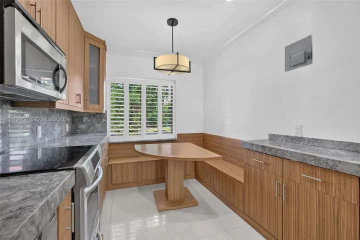 Kitchen featuring wood-finish cabinetry, stone-surface countertops, built-in breakfast nook with integrated bench seating, polished tile flooring, and shutter window treatments