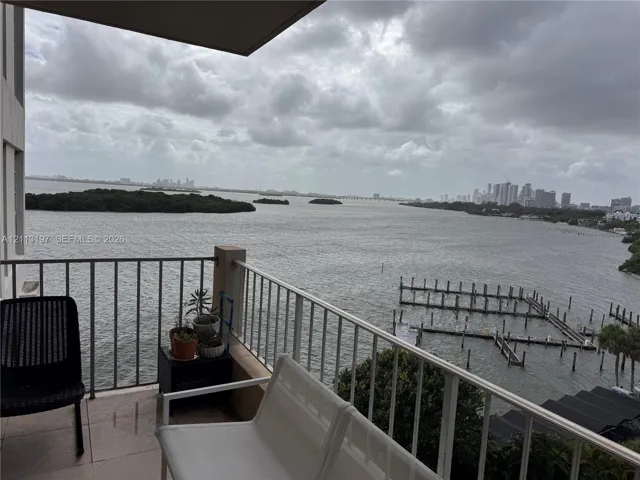 Covered balcony featuring tile flooring and metal railings overlooking the bay, shoreline, and city skyline