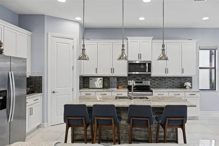 Beautiful kitchen featuring white shaker-style cabinetry, & stone-surface center island & stylish over counter pendant lighting.
