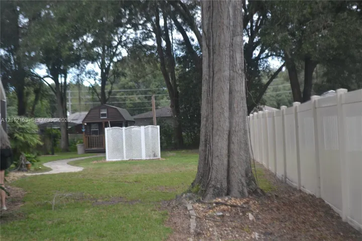 Backyard featuring a privacy fence, stone-finish walkway, detached storage structure, and mature trees