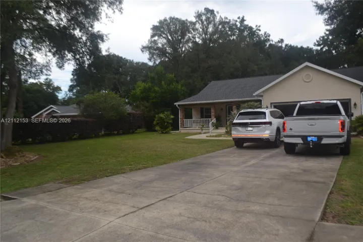 Single-story exterior featuring a concrete driveway, two-car garage, covered front porch, and mature landscaping