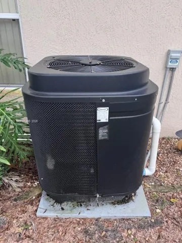 Exterior HVAC condenser unit featuring a black metal protective grill, solid casing, and reinforced base pad