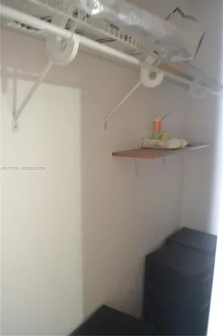 Storage area featuring a wall-mounted wire shelf with an integrated hanging rod and an additional wood-finish shelf