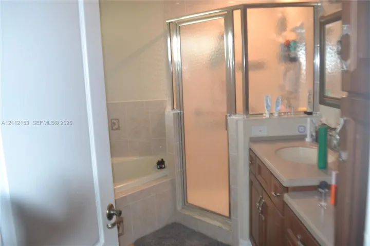 Bathroom featuring a soaking tub with tile surround, a glass-enclosed shower, a wood-finish vanity with a stone-composite countertop, and a recessed vanity mirror