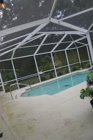 Screened-in patio enclosure featuring a swimming pool with integrated steps and a metal handrail