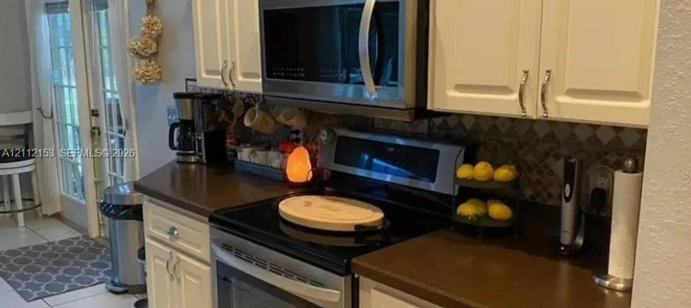 Kitchen featuring white cabinetry, solid-surface countertops, decorative stone tile backsplash, stainless steel over-the-range microwave, and glass-paned double doors