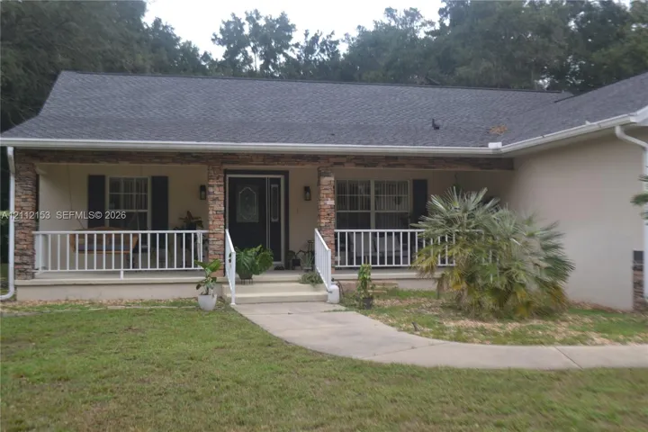 Exterior facade featuring stone veneer columns, a covered front porch, white railings, and a shingle roof