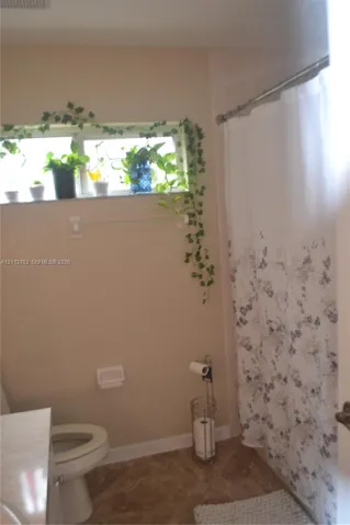 Bathroom featuring a horizontal window with stone sill, ceramic tile flooring, and a metal shower rod
