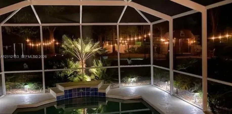 Screened-in enclosure with a concrete deck, built-in raised pool step with decorative tile detailing, and integrated landscape lighting