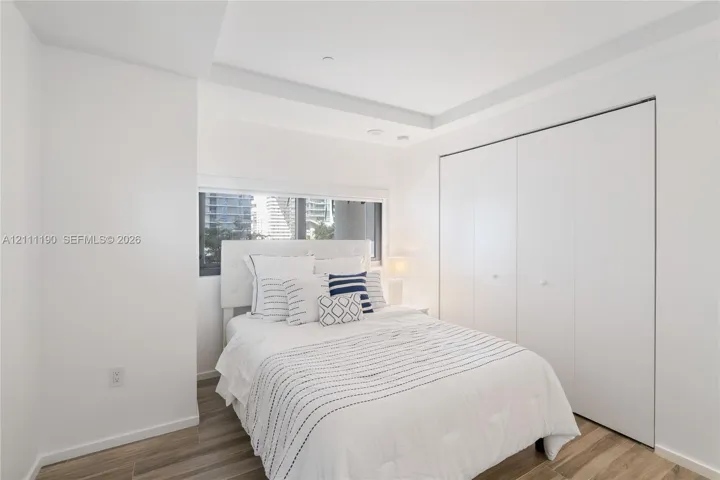 Recessed tray ceiling, horizontal sliding window, and floor-to-ceiling closet with white panel doors, complemented by wood-finish flooring
