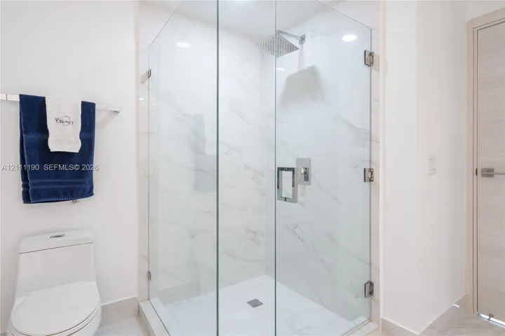 Walk-in shower featuring a frameless glass enclosure, floor-to-ceiling stone-finish tile surround, wall-mounted polished chrome fixtures, and a ceiling-mounted rainfall showerhead