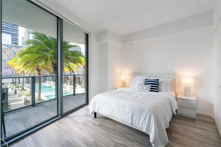Floor-to-ceiling glass sliding doors, private balcony with metal railing, wood-finish flooring, and neutral wall finishes