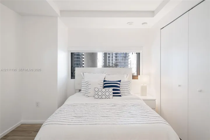 Tray ceiling, horizontal window, and floor-to-ceiling closet with dual-panel doors, featuring wood-finish flooring