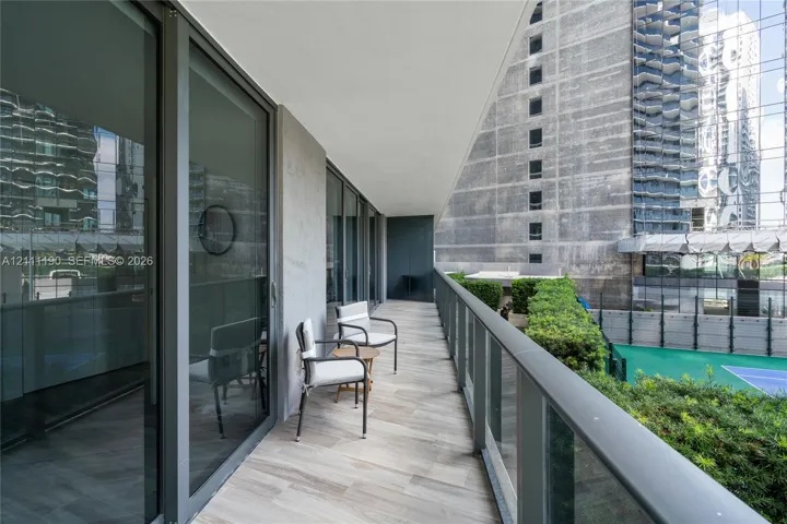 Covered balcony featuring wood-finish tile flooring, full-height sliding glass doors, and a glass-paneled railing