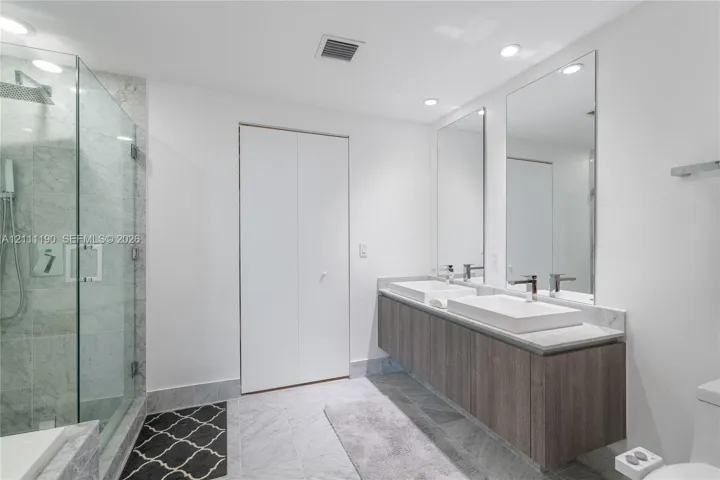 Floating dual-vanity with stone countertop, rectangular vessel sinks, floor-to-ceiling glass-enclosed shower, stone-tile flooring, and full-height wall mirrors