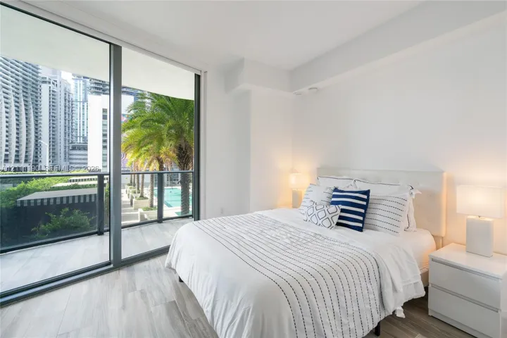 Floor-to-ceiling glass sliding doors, private balcony with metal railing, and wood-finish flooring