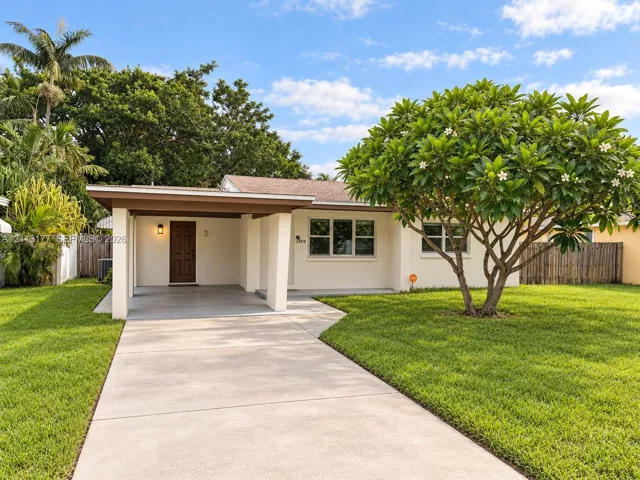 Exterior facade featuring a covered carport, concrete driveway, and expansive lawn with mature landscaping