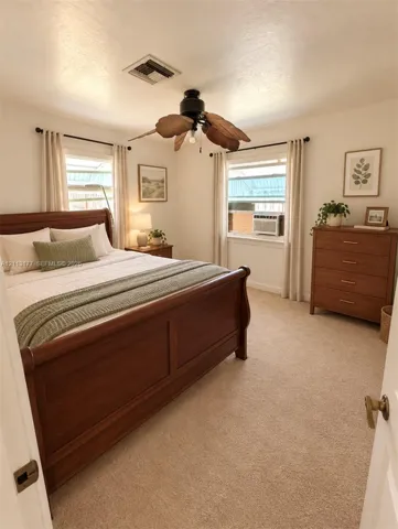 Neutral-toned carpeting, dual windows with curtain rods, and a ceiling fan with leaf-shaped blades